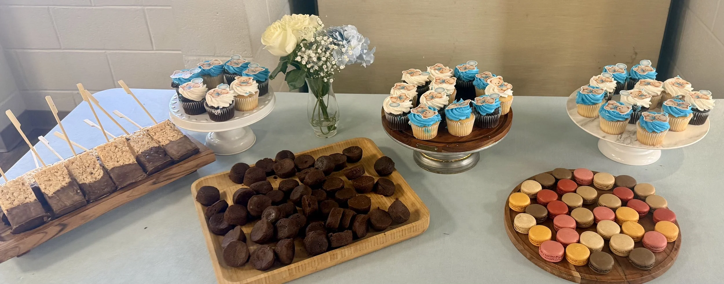 Dessert table with brownies, rice crispies, macarons, and blue and white cupcakes with a flower vase (blue and white flowers)