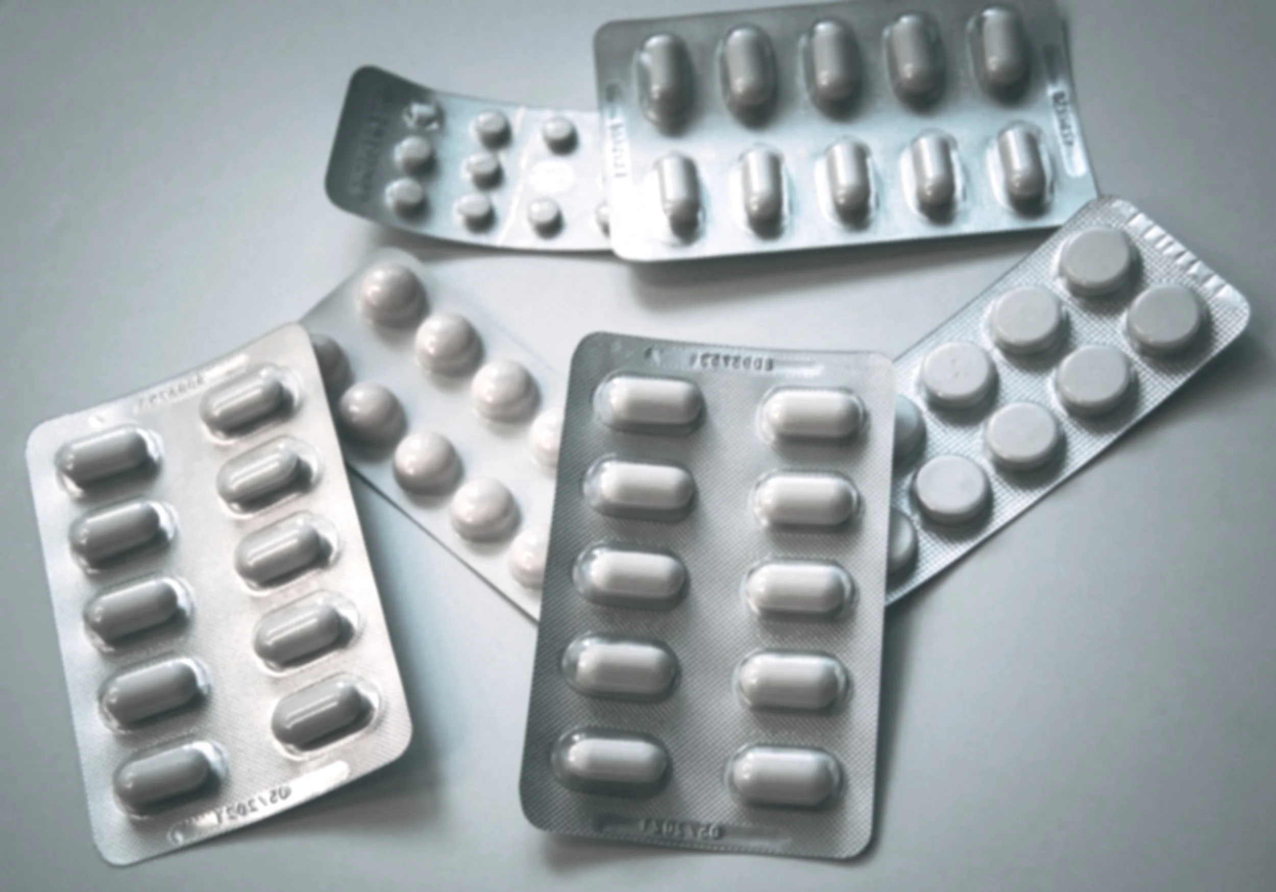 Multiple blister packs of white pills or capsules on a gray surface.
