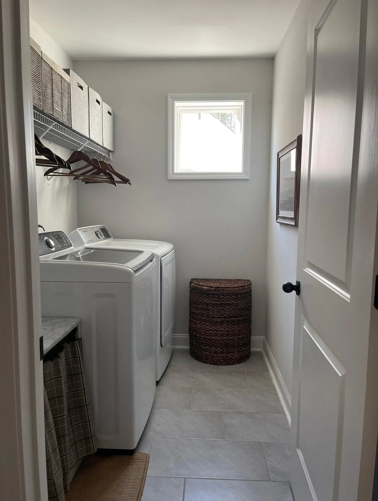 Laundry room with washer and dryer, a small window, storage baskets, and a laundry bin.
