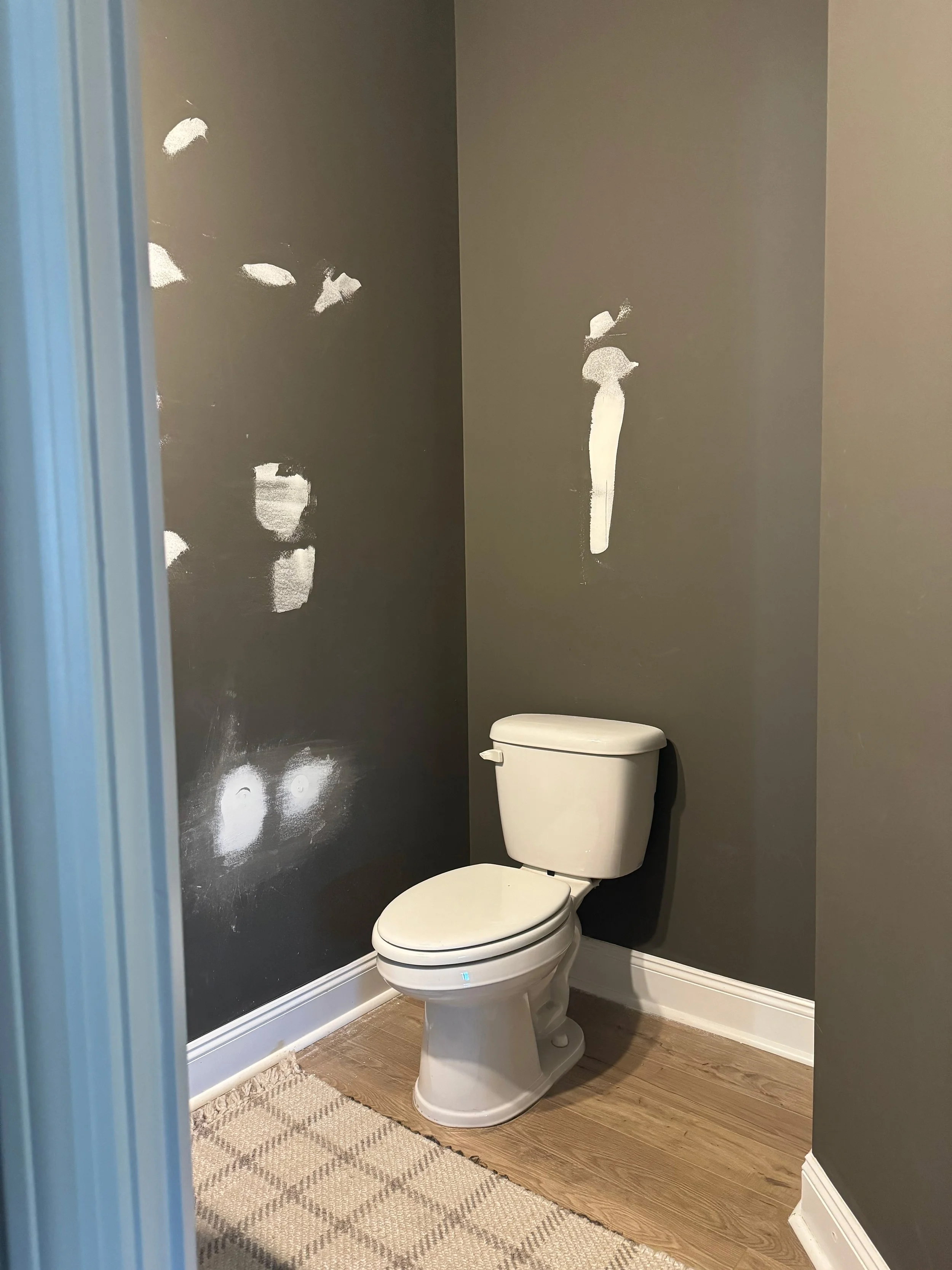 A small bathroom with a white toilet against a dark gray wall that has white paint marks.