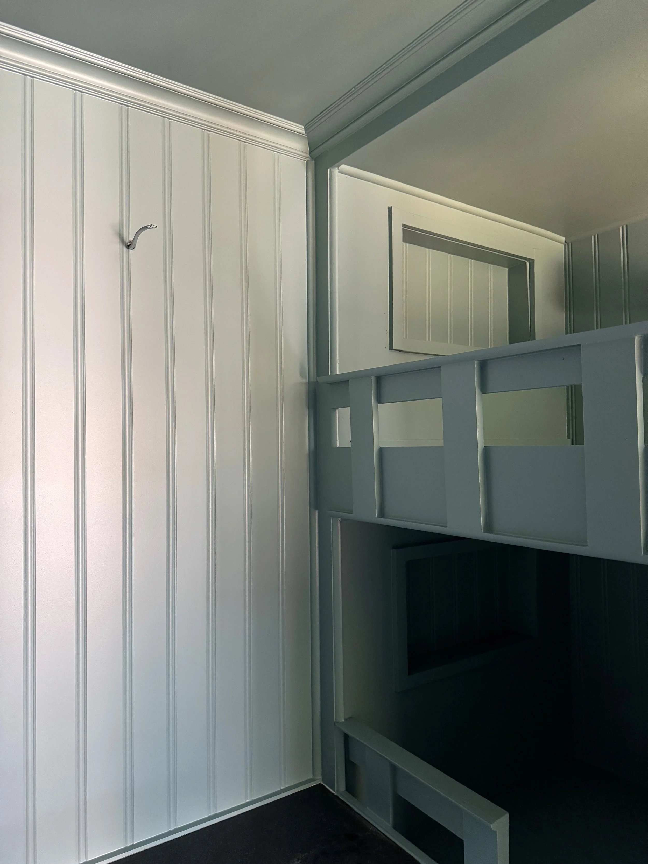 Empty white-painted wooden bunk bed frame with a ladder and built-in storage, against white paneled walls in a room.