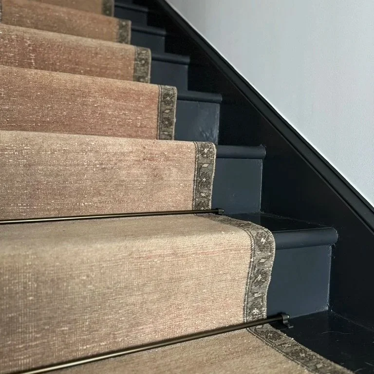 Close-up view of a staircase with beige carpeted steps and black metal stair rods.
