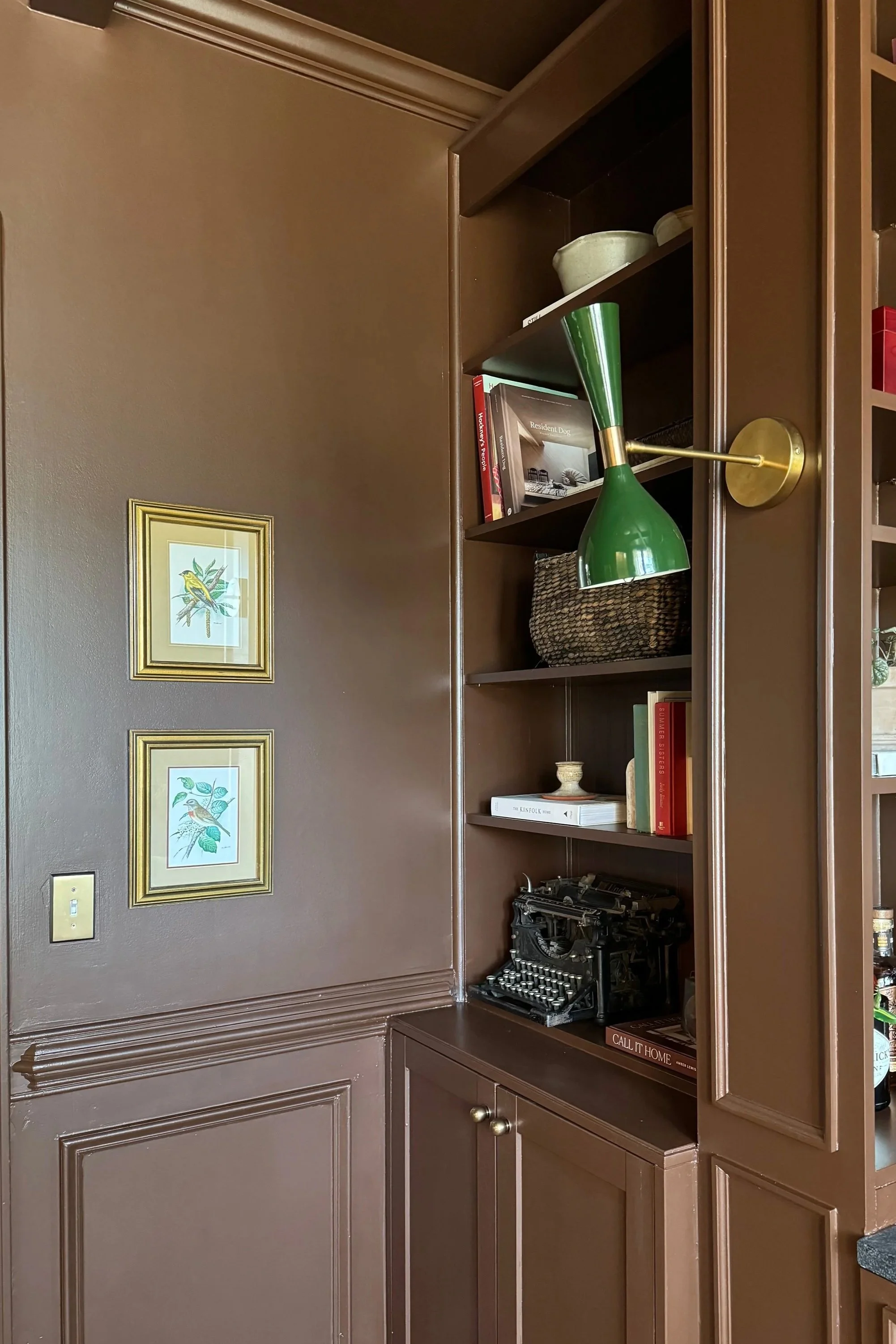 Brown built-in bookshelf with decorative items and a vintage typewriter in a room with dark brown walls.