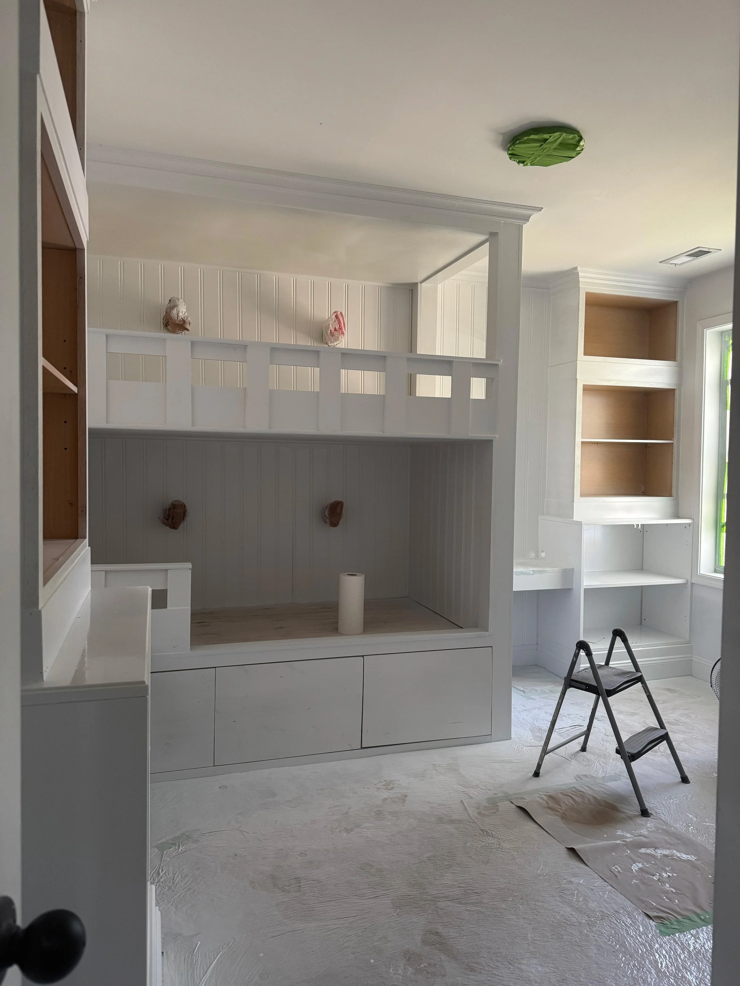 Room under renovation with white cabinetry, a step ladder, and an unfinished wall with open shelves.