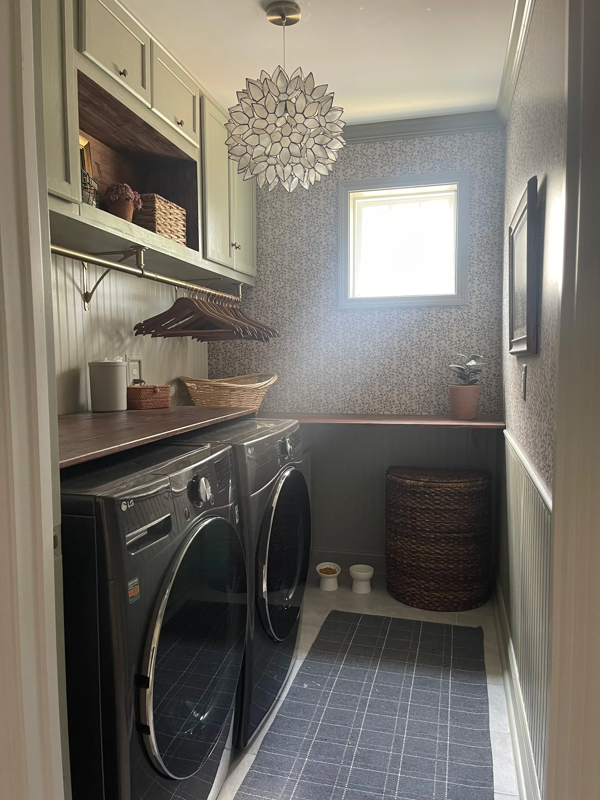 A laundry room with a front-loading washer and dryer, shelves above with baskets, and a window allowing natural light.