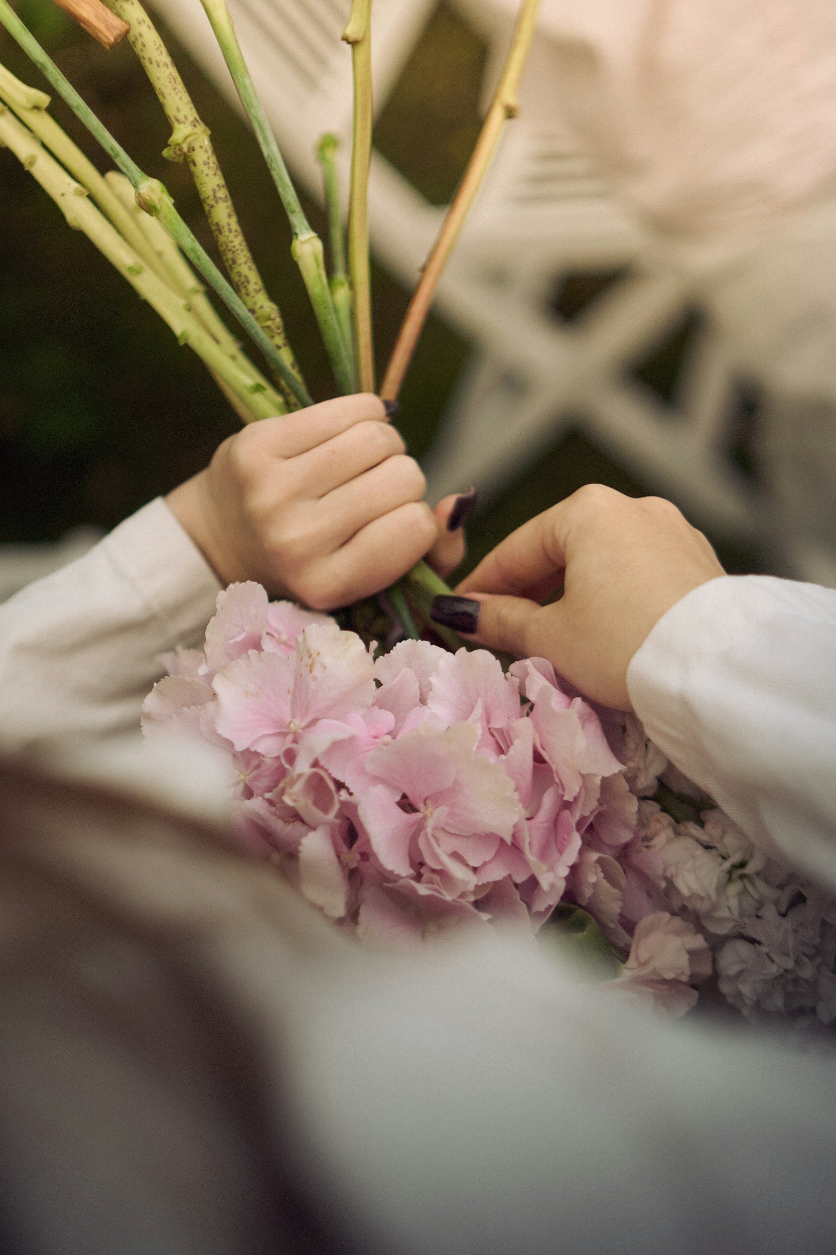 A person is holding green floral stems while arranging pink hydrangea flowers.