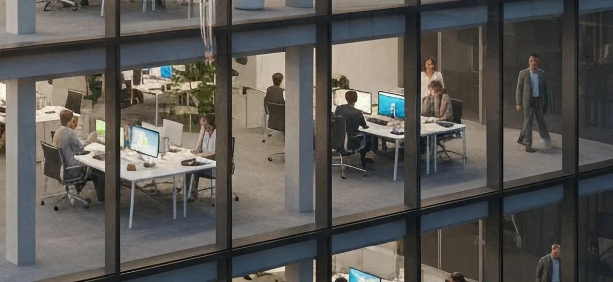 Office workers working at desks with computers in a glass-walled office building during daytime.