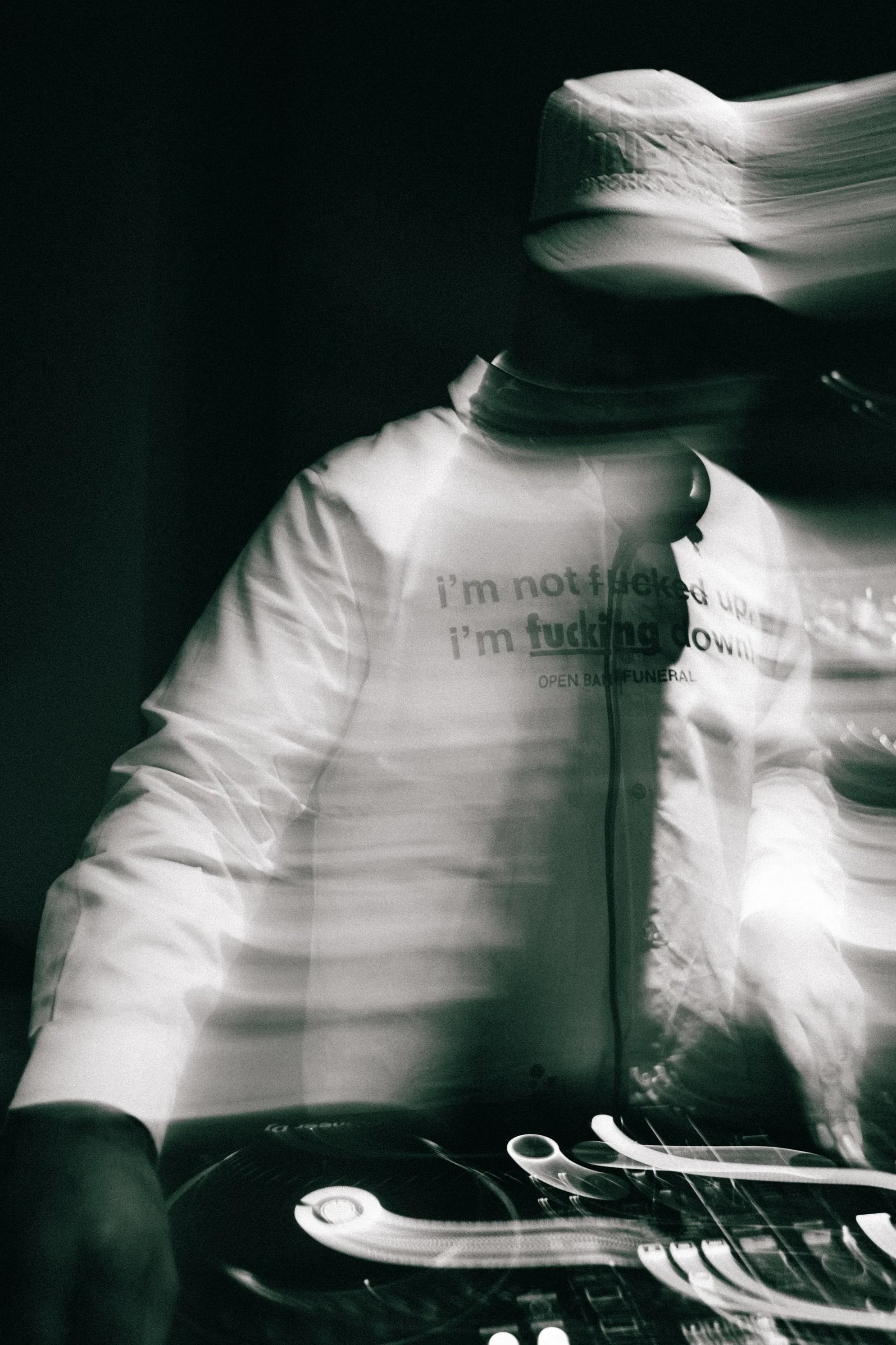 A male DJ  wearing a bucket hat and a t-shirt with text, standing in front of a camera, captured with motion blur and light streaks effects.