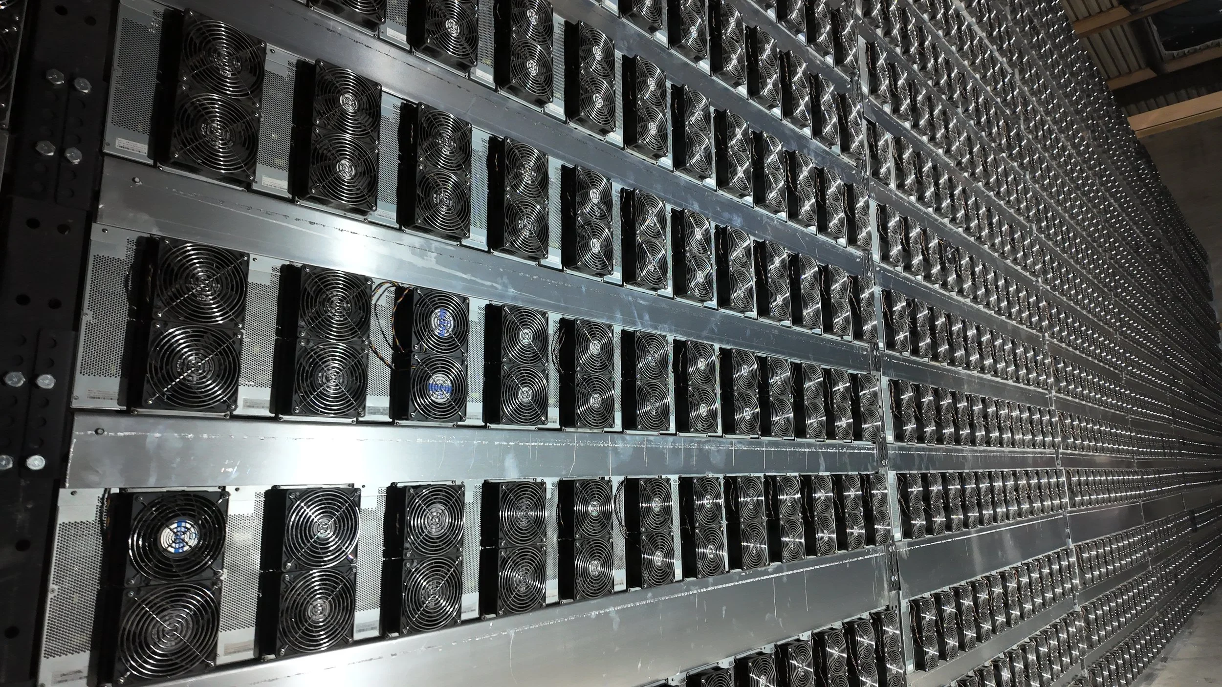 Row of cryptocurrency mining hardware with multiple cooling fans installed in a mining farm.