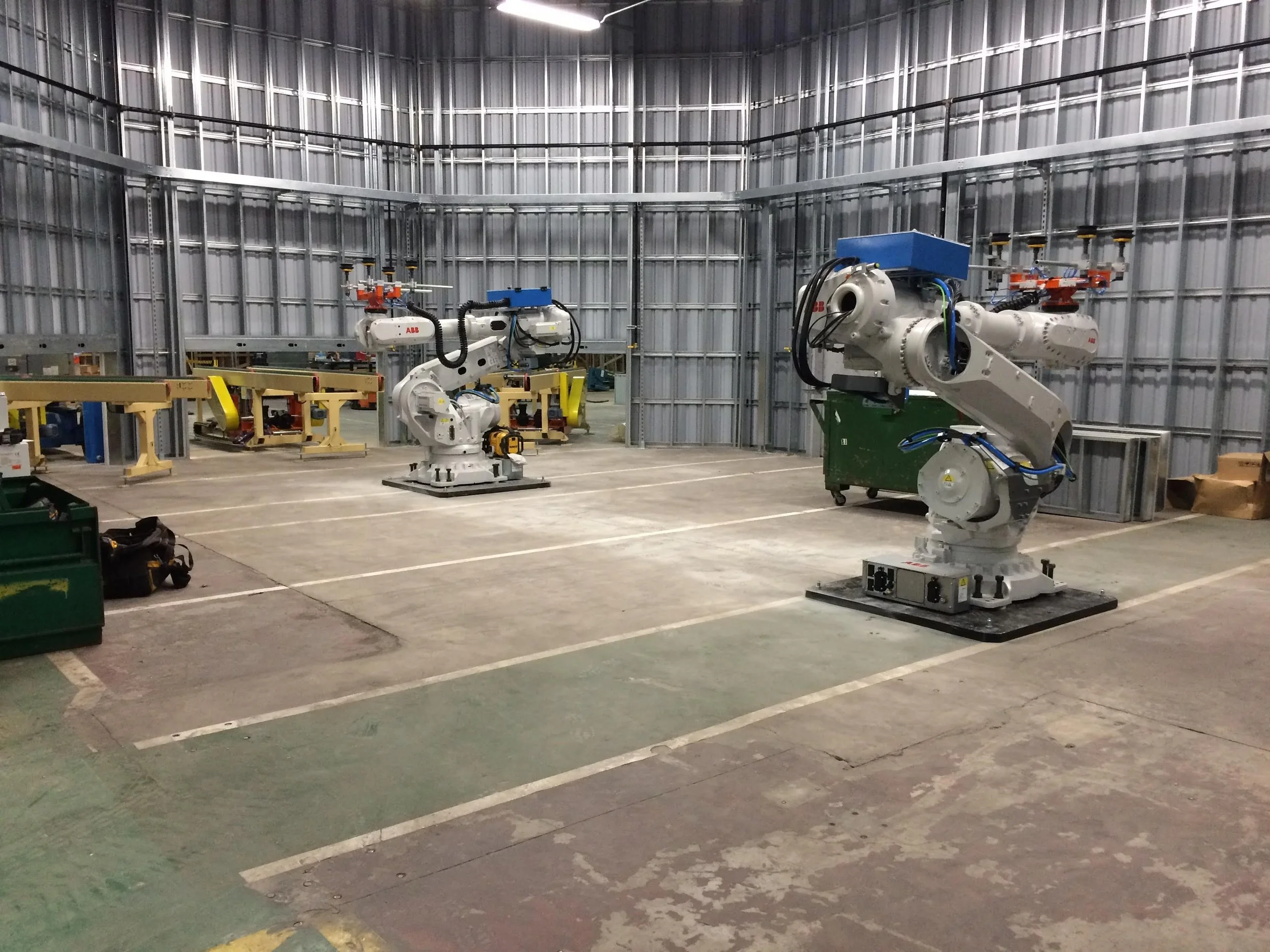 Industrial robotic arms in a metal-walled workshop or factory space.