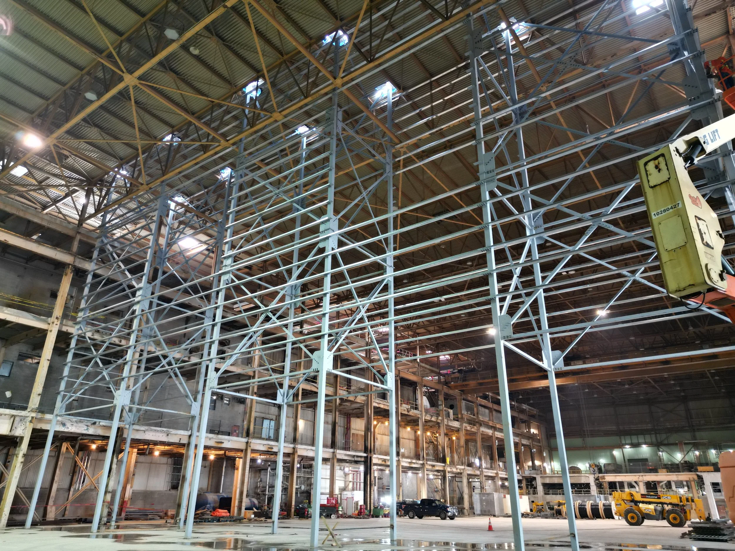 Interior view of a large industrial warehouse under construction, showing steel framework and construction equipment.