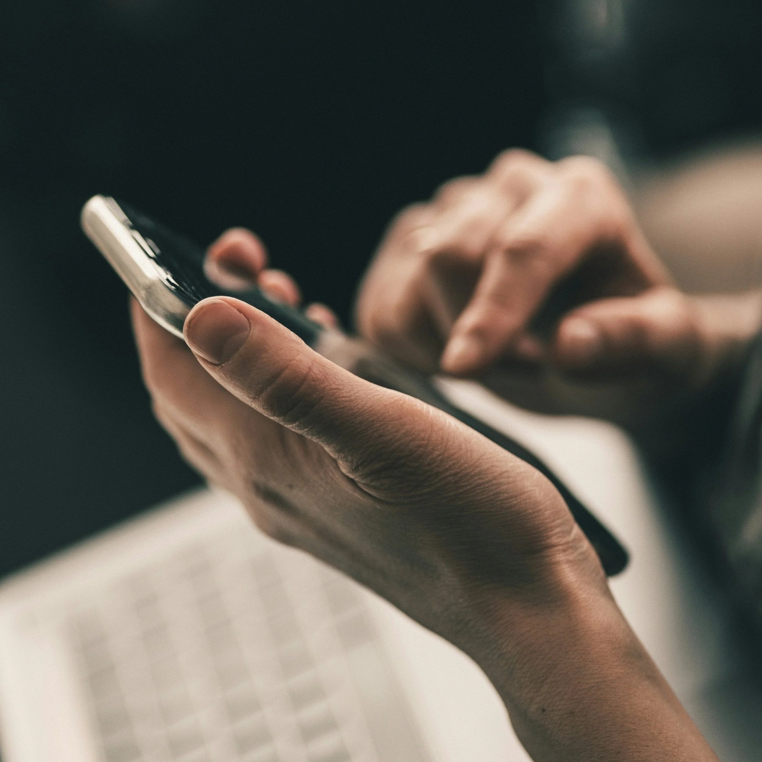 Close-up of a person's hands using a smartphone, holding it with one hand and touching the screen with the other.