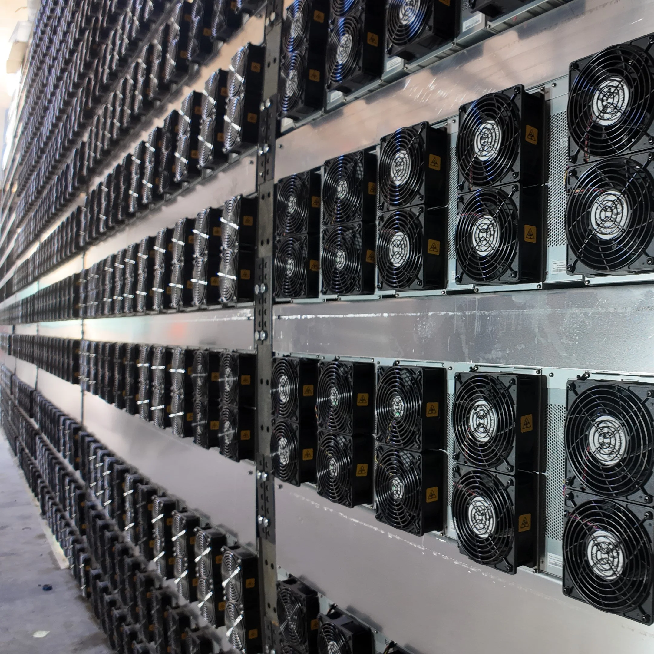 Rows of cryptocurrency mining hardware with cooling fans mounted on metal racks.