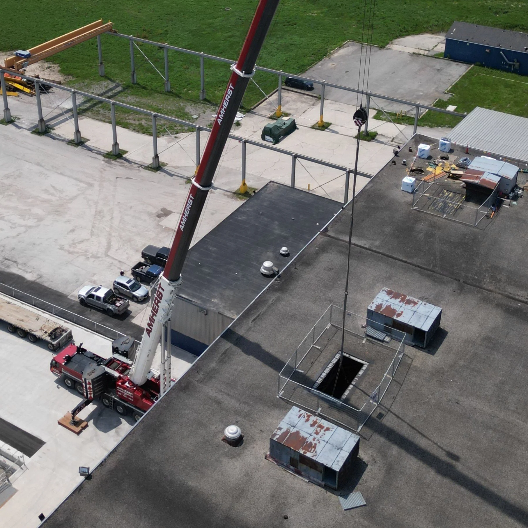 A construction crane lifting a large metal object on a rooftop with various pieces of equipment and debris scattered around.