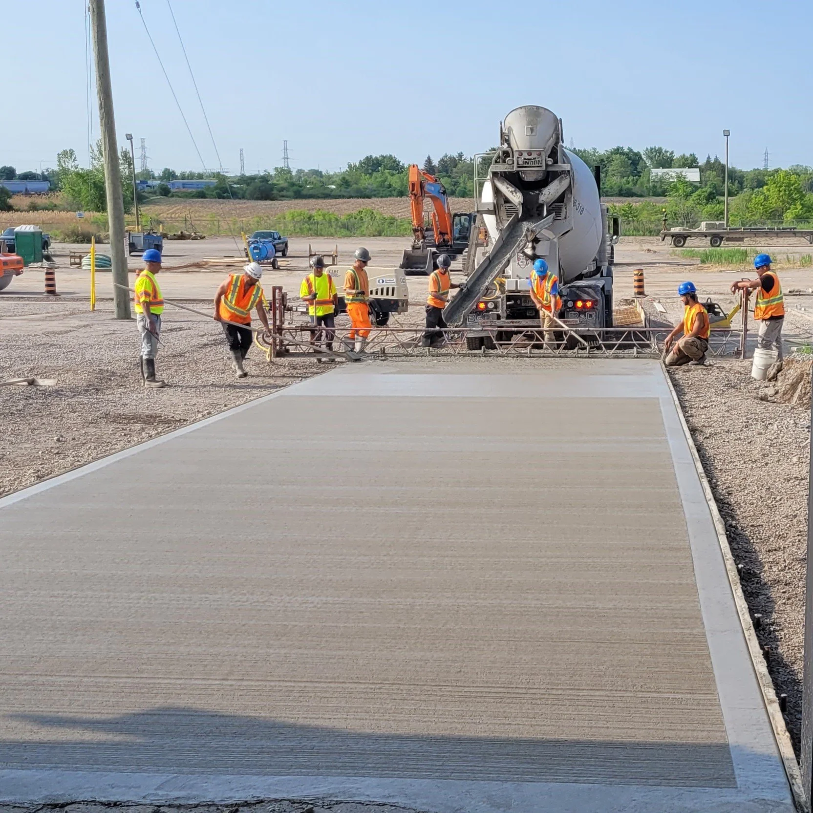 Construction workers in safety vests and helmets pouring and finishing concrete on a new sidewalk at a construction site.