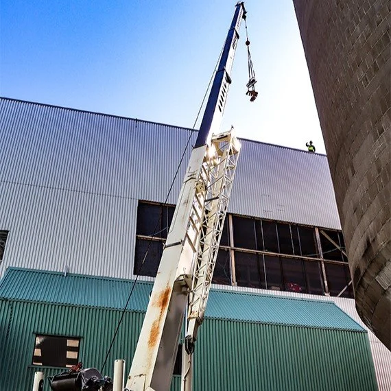 Construction crane lifting materials at a building site with workers on the roof, blue sky overhead