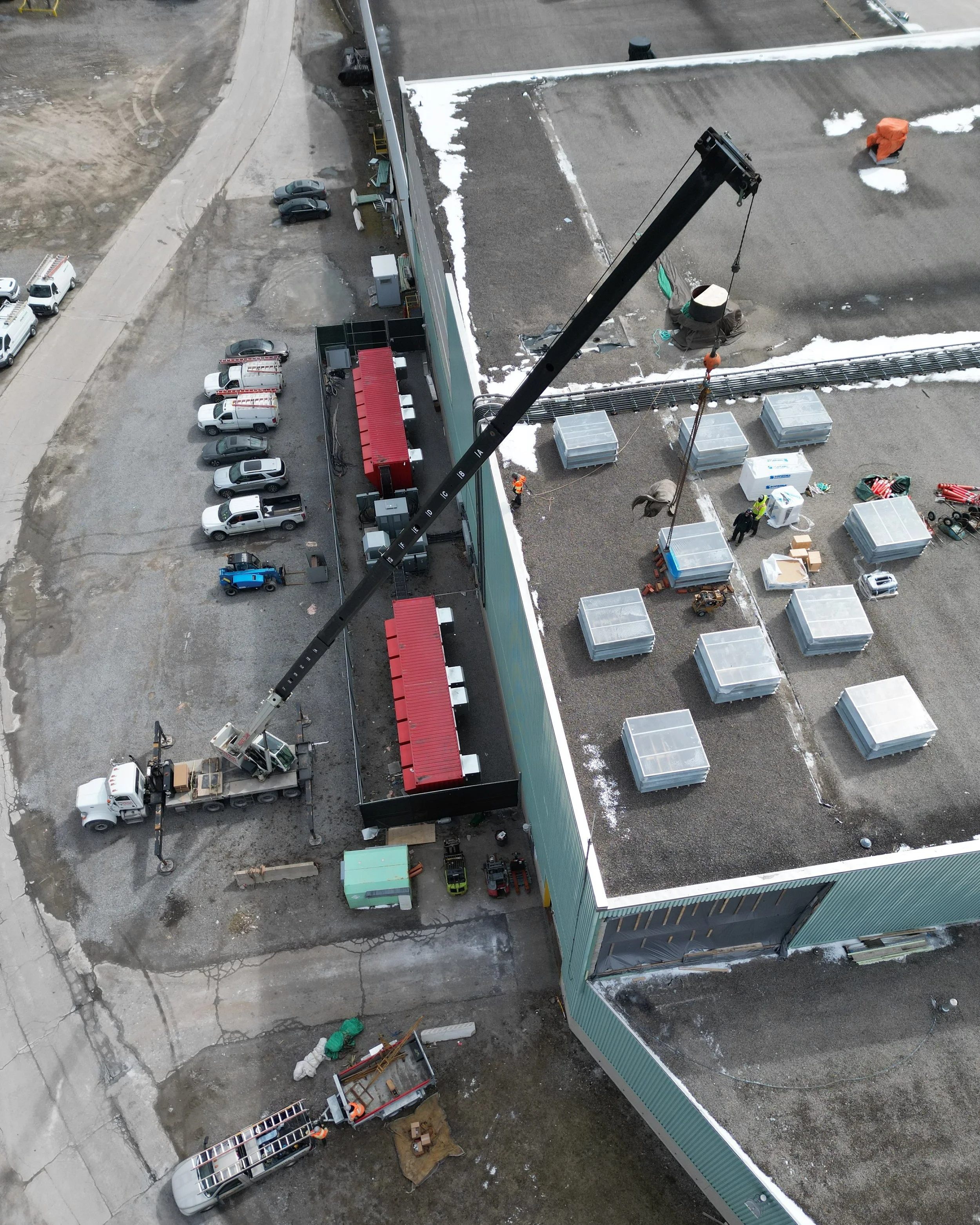 Aerial view of a construction site on a rooftop, with workers, equipment, and a crane lifting materials.