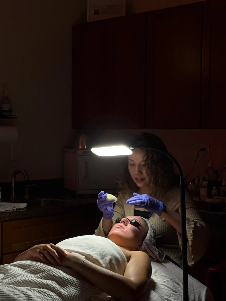 A woman lying on a treatment bed at a Day Spa Surprise AZ, Med Spa Surprise AZ, receiving a facial with protective sunglasses