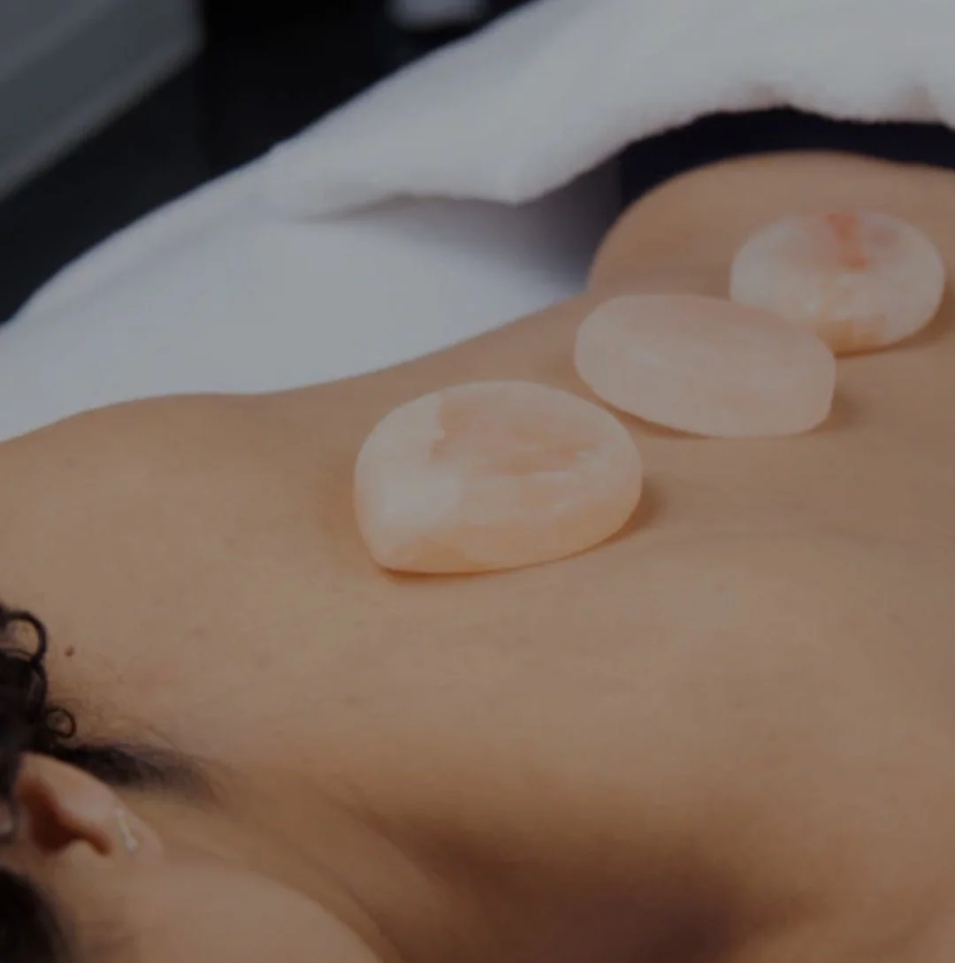 Woman receiving hot stone massage, with four smooth, oval-shaped stones placed on her back.