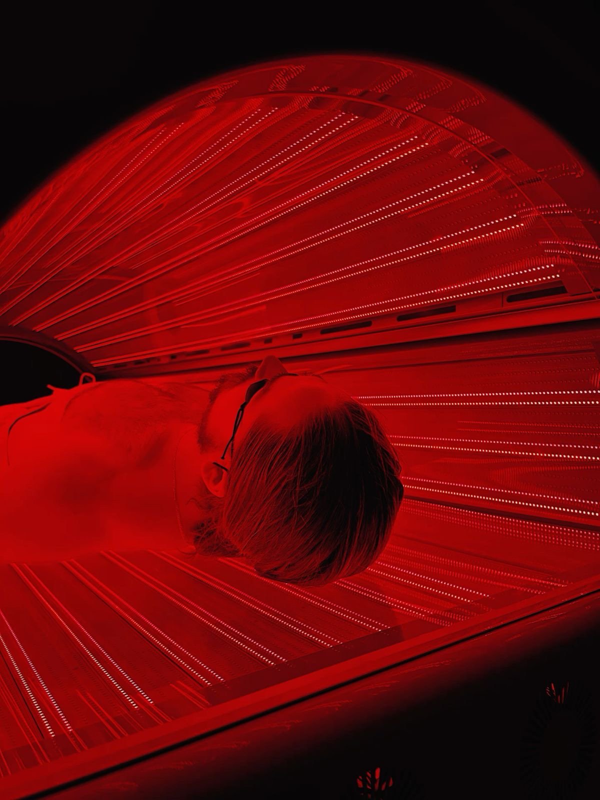 A person relaxing in a full body red light therapy Surprise AZ treatment bed, surrounded by soft glowing red panels in a wellness setting.