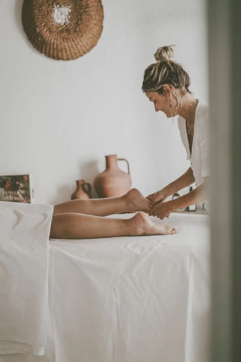 Close-up of a person's hand placing a black stone on a person's back during a massage or hot stone therapy, with warm candlelight in the background.