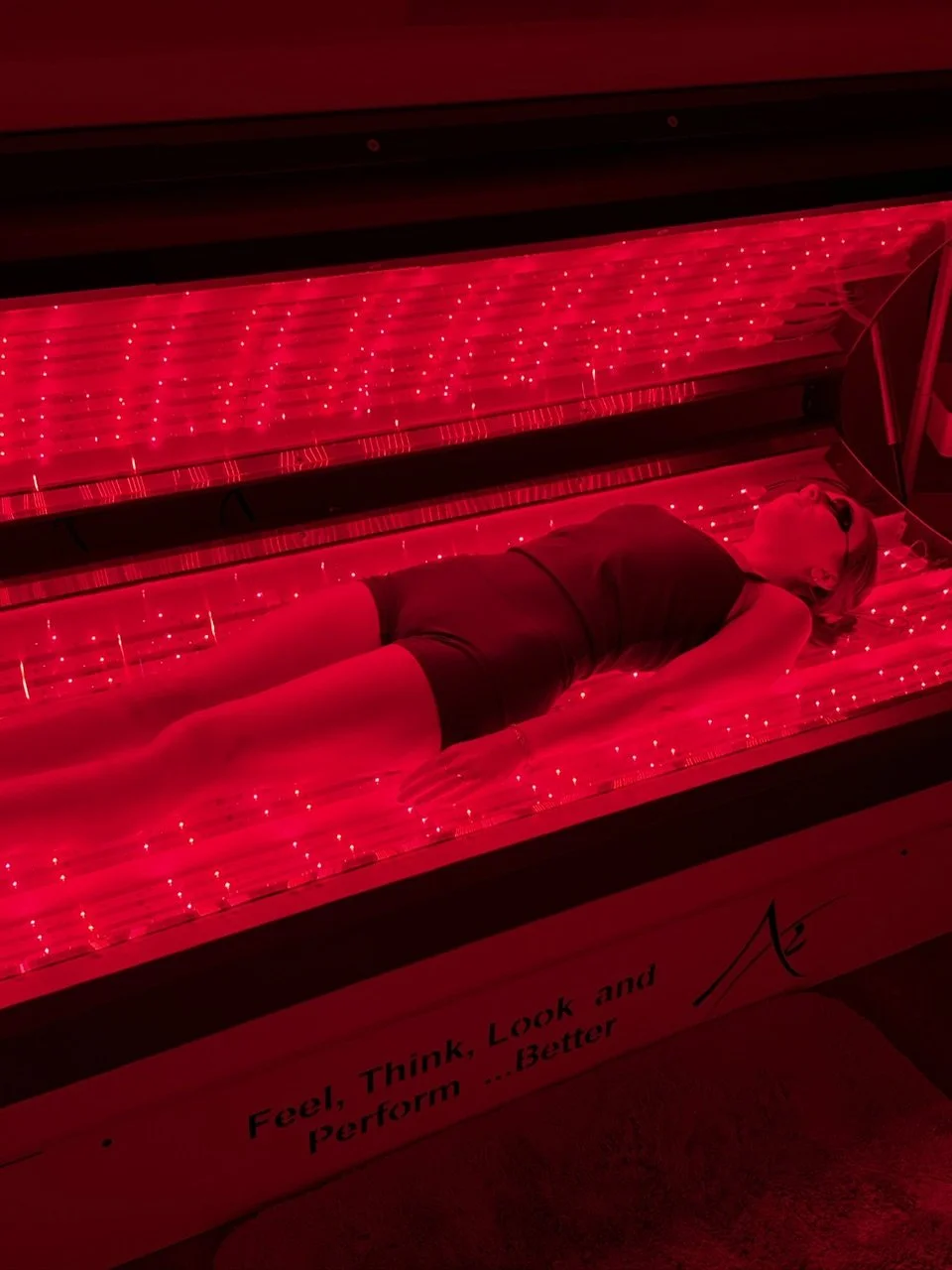 Person inside a Day Spa Surprise AZ, Med Spa Surprise AZ red light therapy bed, wearing black clothing and sunglasses.