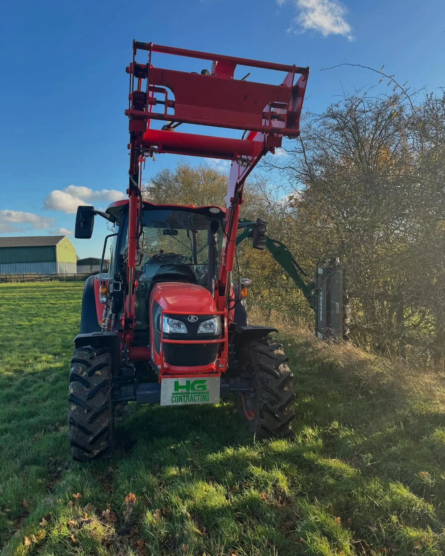 Red tractor on grassy field with a boom lift attachment raised in a sunny outdoor setting.