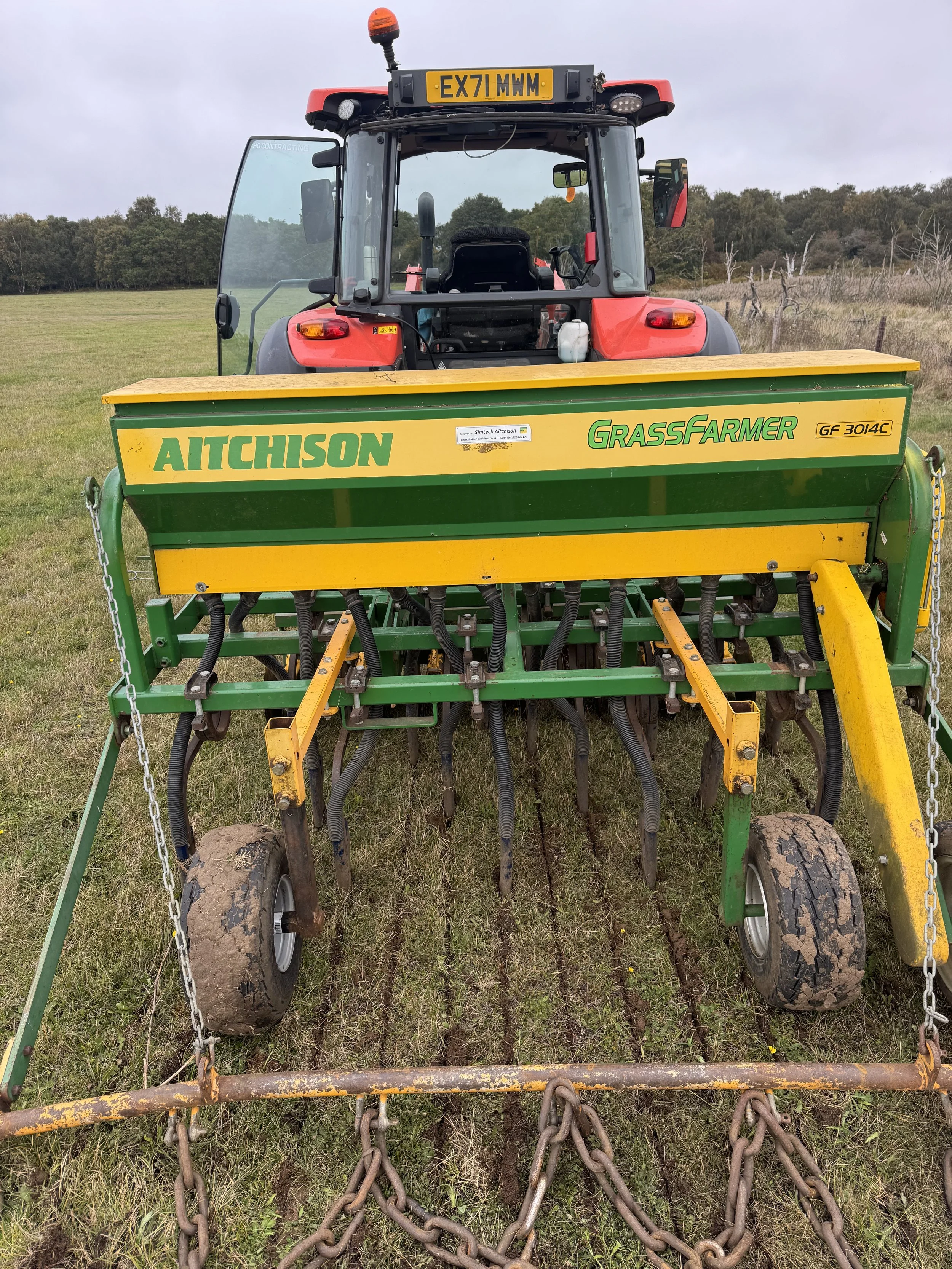A tractor with a grass seeder attachment in a grassy field.