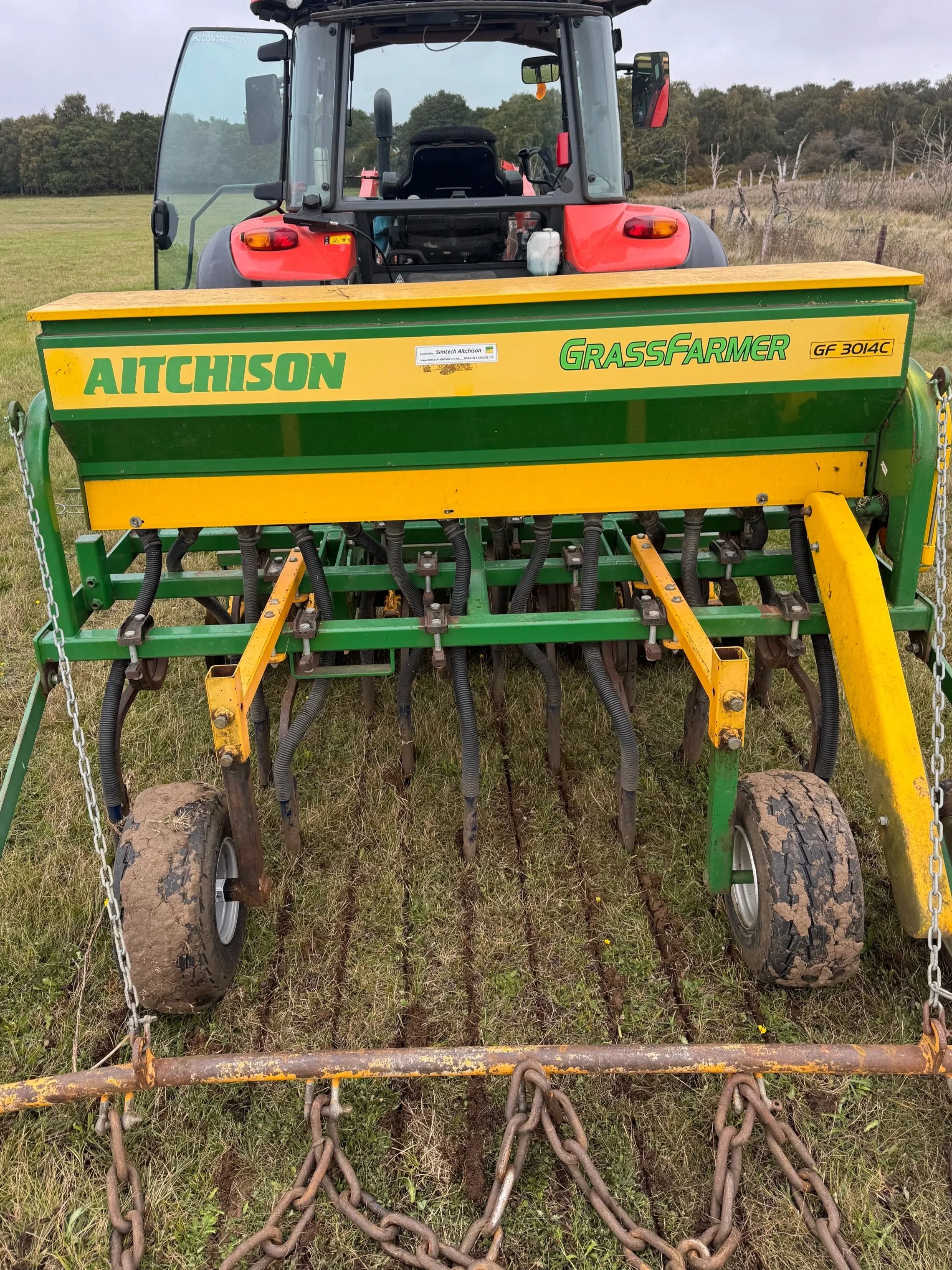A tractor pulling a grass seeder on a grassy field.