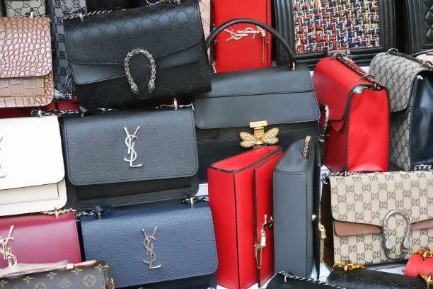 A display of various handbags, including designer brands like Yves Saint Laurent, Gucci, and others, arranged on a store shelf.