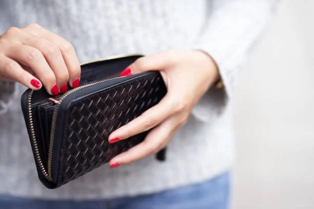 Person holding a black woven leather wallet with a zipper and red nail polish.