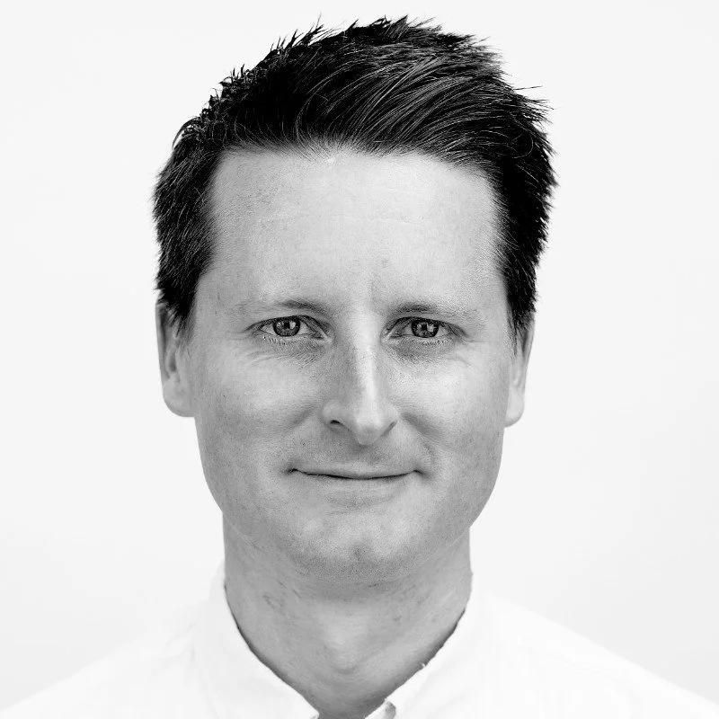 Mike Clear Clear, co-founder of Made Clear Studios. Black and white headshot of a man with short dark hair, wearing a white collared shirt, smiling slightly, against a plain light background.