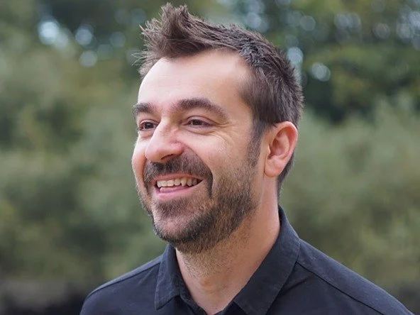 Dave Kaye, founder of FieldNotes. A smiling man with short, dark hair and a beard, wearing a black shirt outdoors with blurred trees in the background.