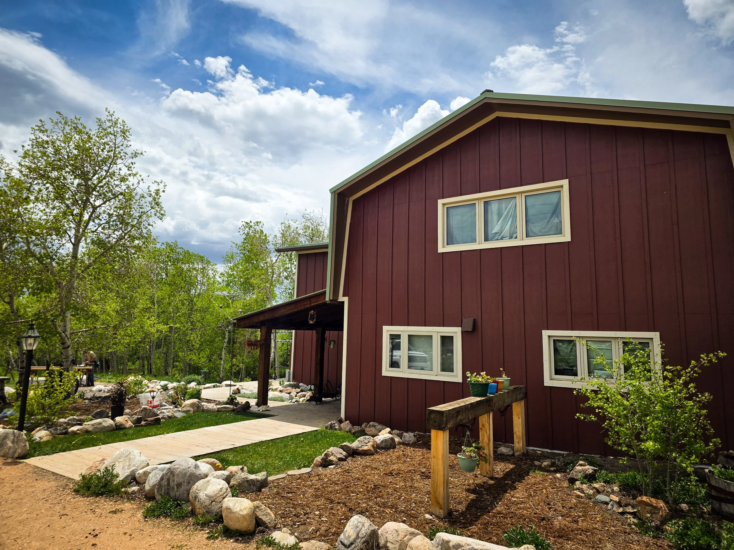A red two-story house with white-framed windows in a lush green yard under a partly cloudy sky.