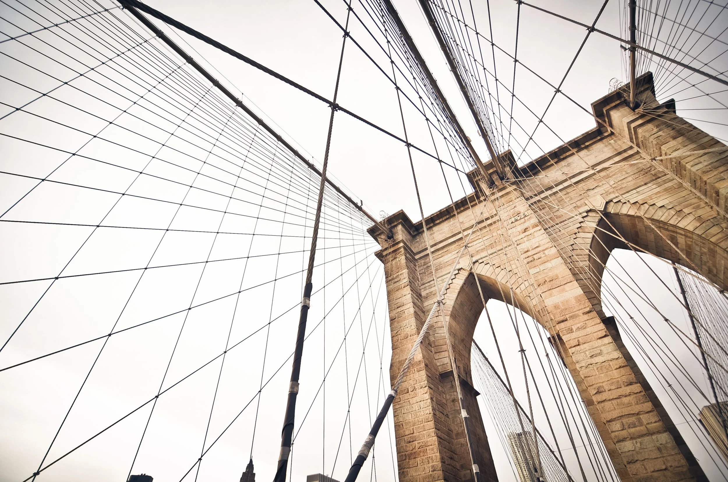 Looking up at the Brooklyn Bridge's stone tower and suspension cables in New York City.