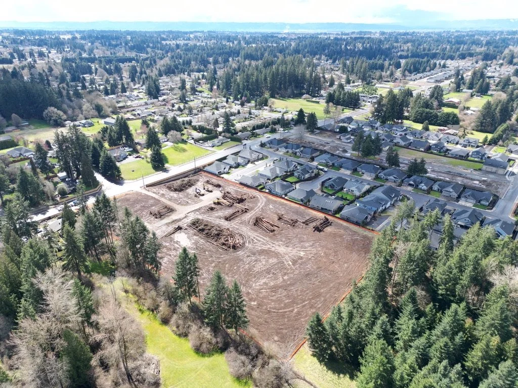Aerial view of a residential neighborhood with a construction site in the foreground, surrounded by trees and houses.
