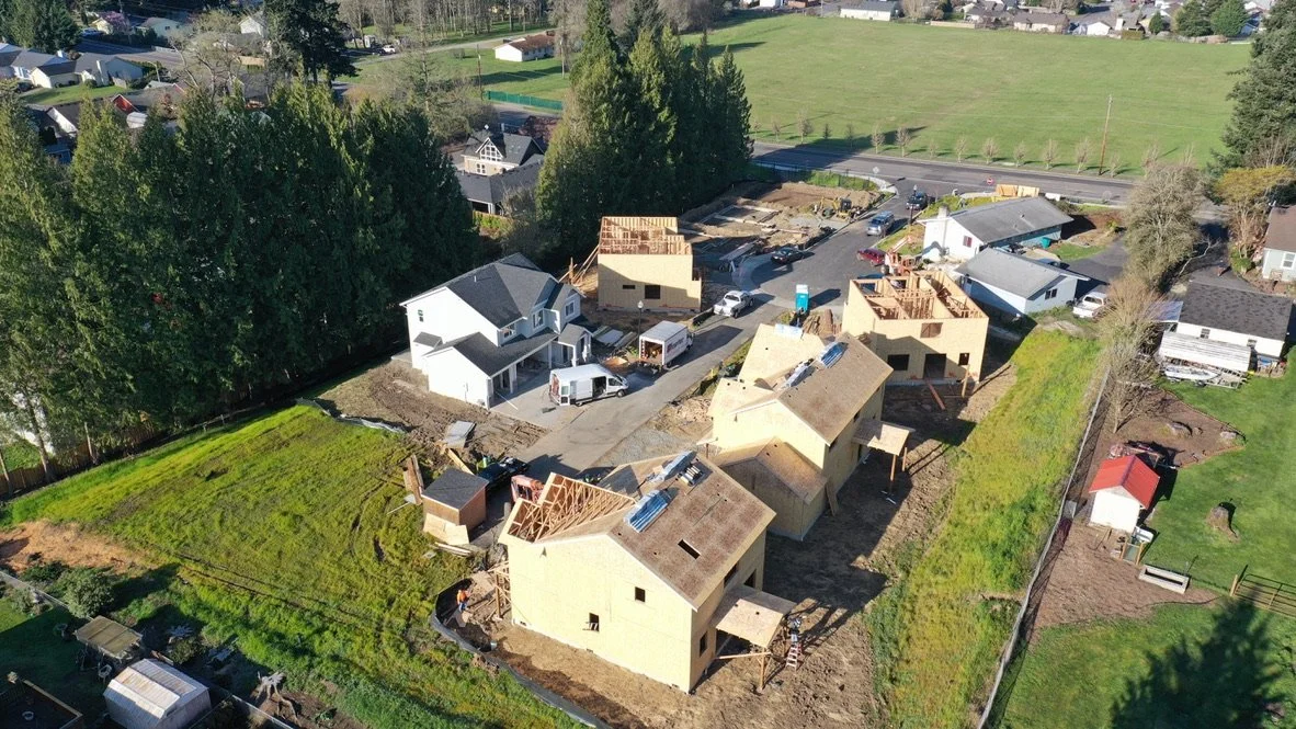 Aerial view of houses under construction with unfinished roofs, some completed homes, and surrounding greenery.