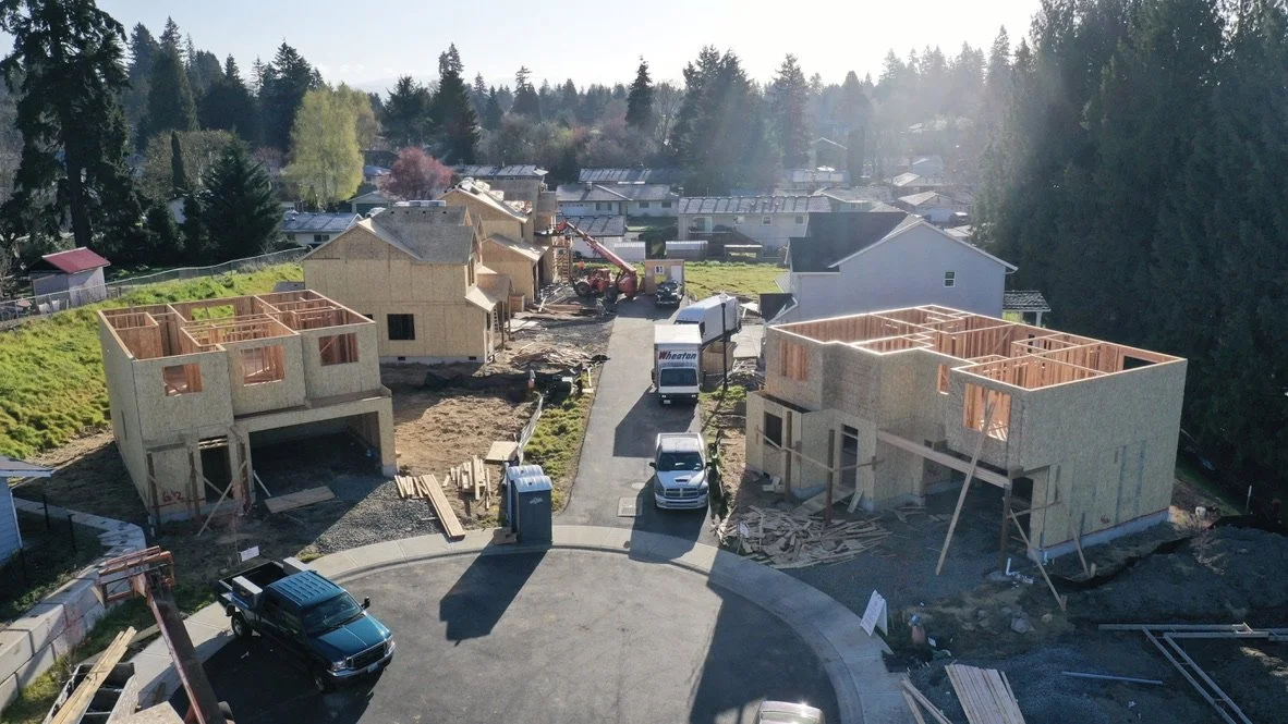 Two houses under construction in a suburban neighborhood with construction vehicles and materials around.