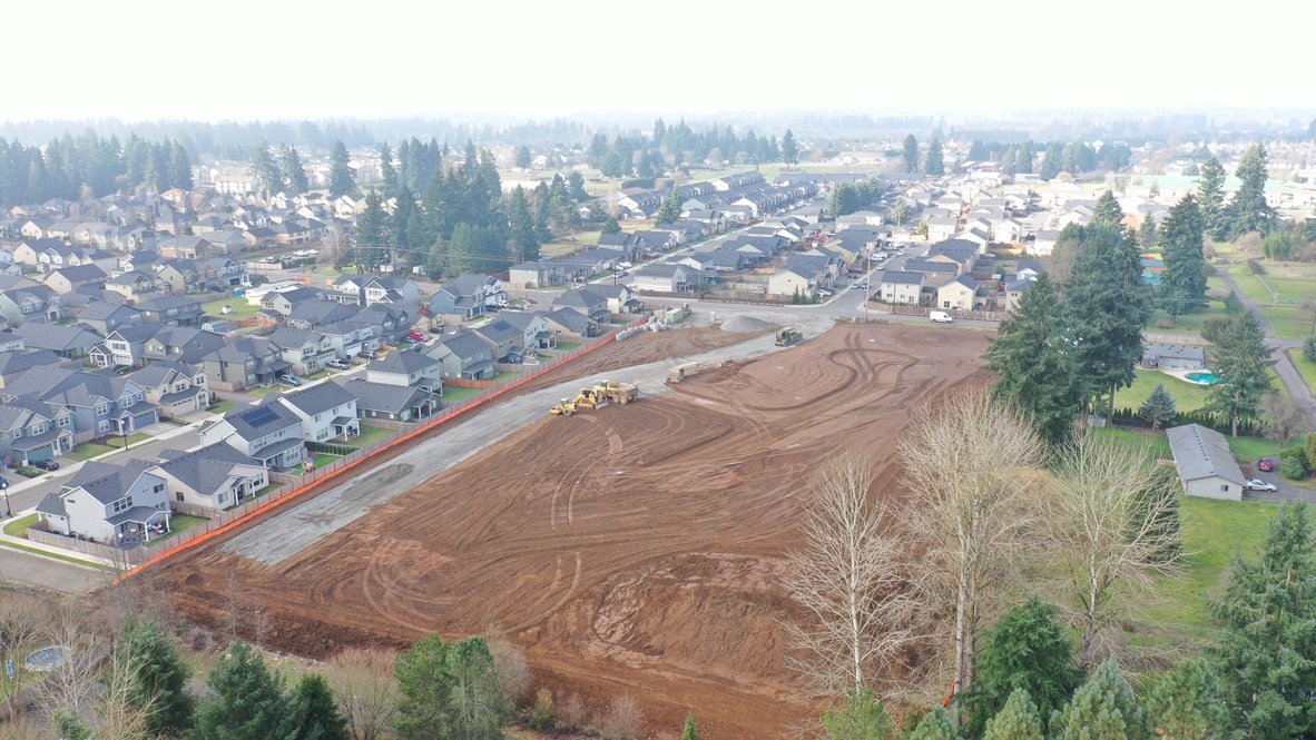 Aerial view of a residential area with houses and a large plot of land under construction, with construction equipment and freshly graded soil.