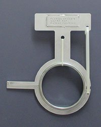 A white plastic circular and T-shaped object with a tube extending from the top right, placed against a gray background.