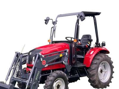 A person operating a red tractor with a large yellow rotary brush attachment on a green golf course.