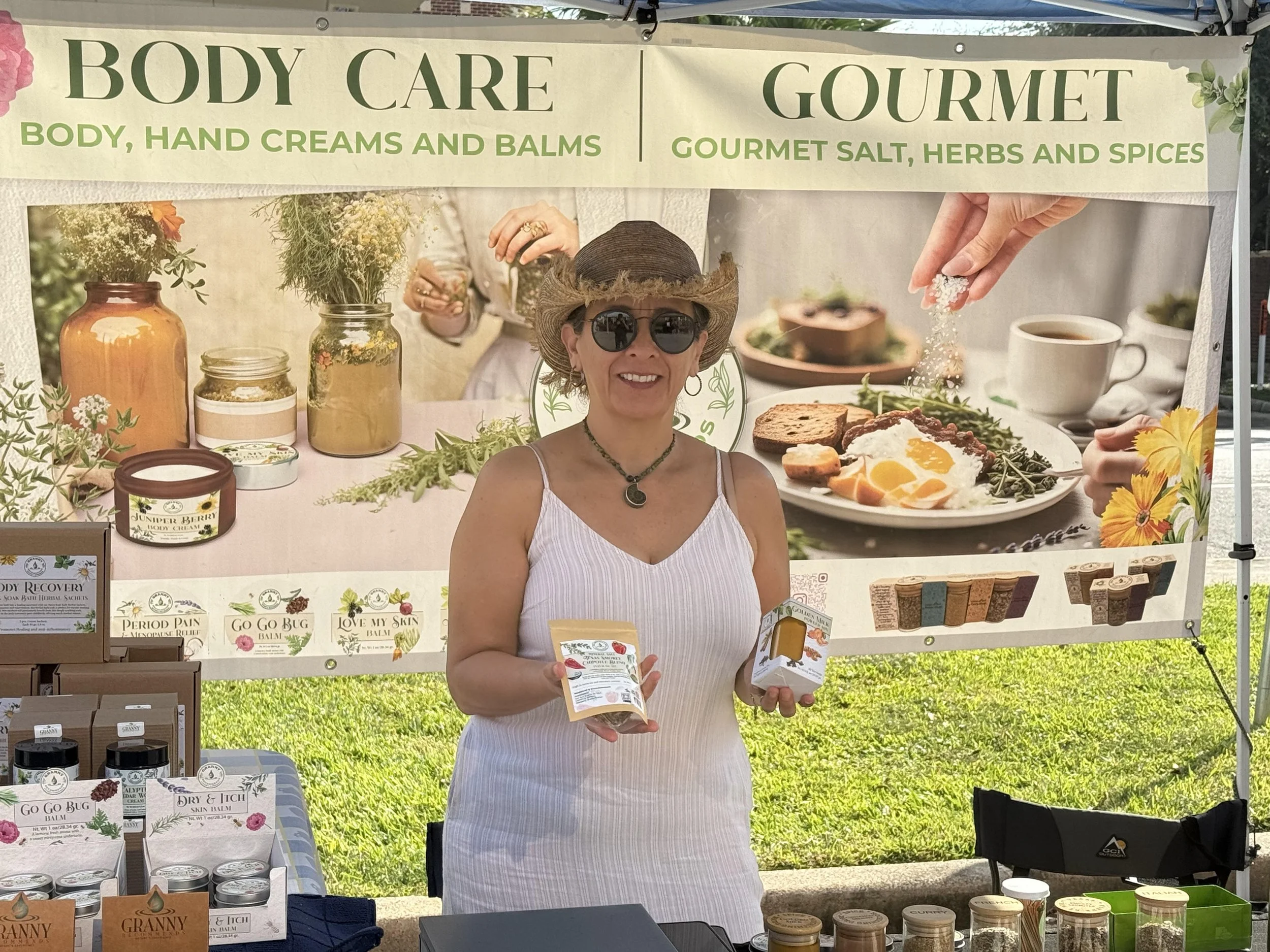 A woman smiling and holding a small container of spice at a booth selling herbs and spices.