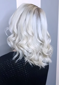 Back view of a woman with shoulder-length, wavy platinum blonde hair wearing a black, dotted top.