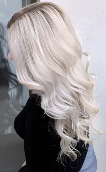 Side view of a woman with long, platinum blonde, wavy hair wearing a black top.
