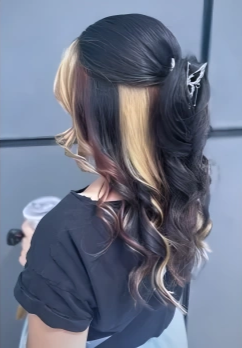 Side view of a woman with multi-colored hair, black, blonde, and pink, styled in loose curls, holding a coffee cup.