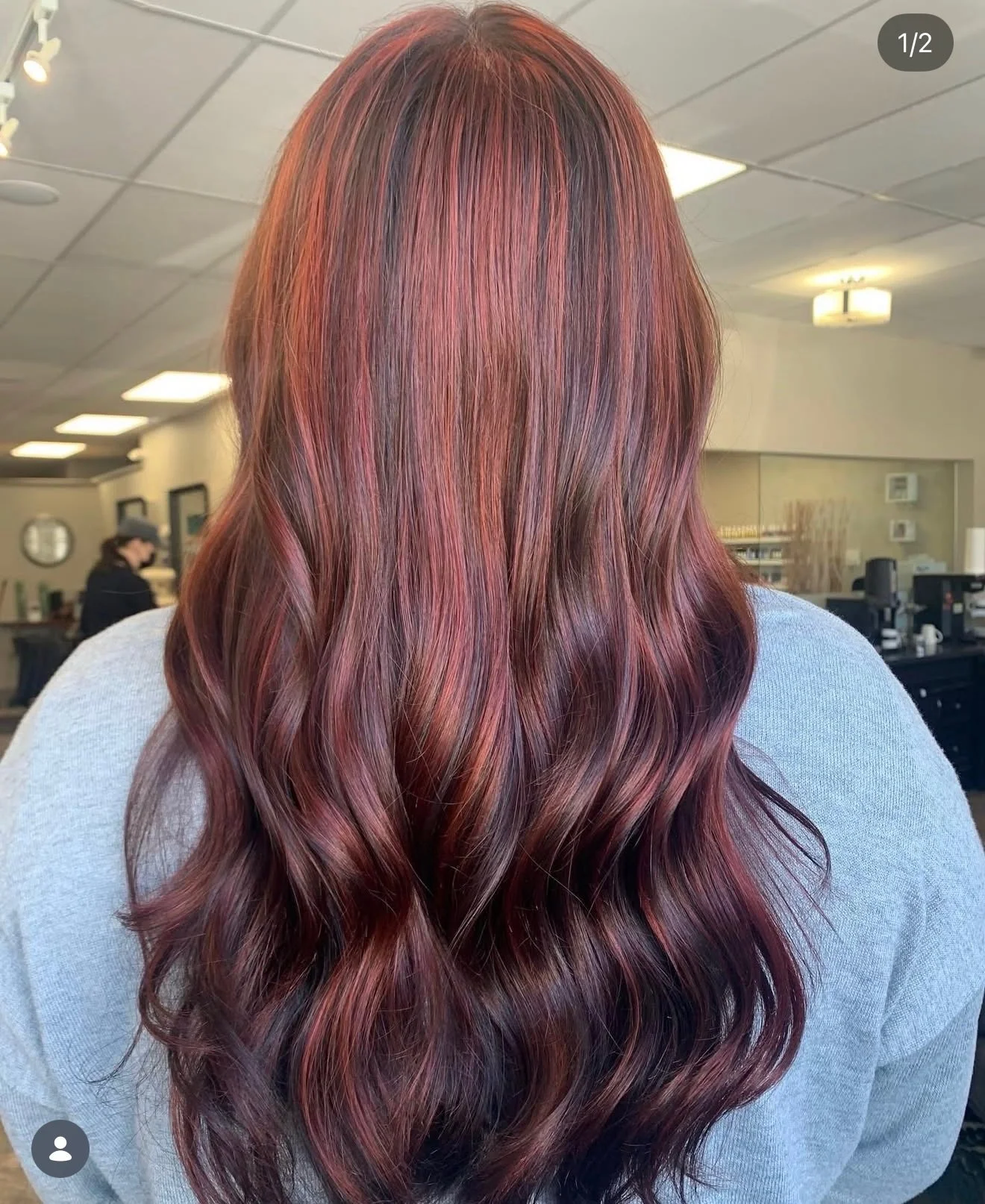 Back view of a woman with long, wavy hair dyed in shades of red and burgundy