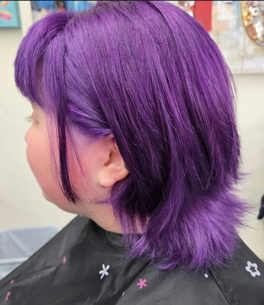 Side view of a person with short, layered, purple hair sitting in a salon chair.