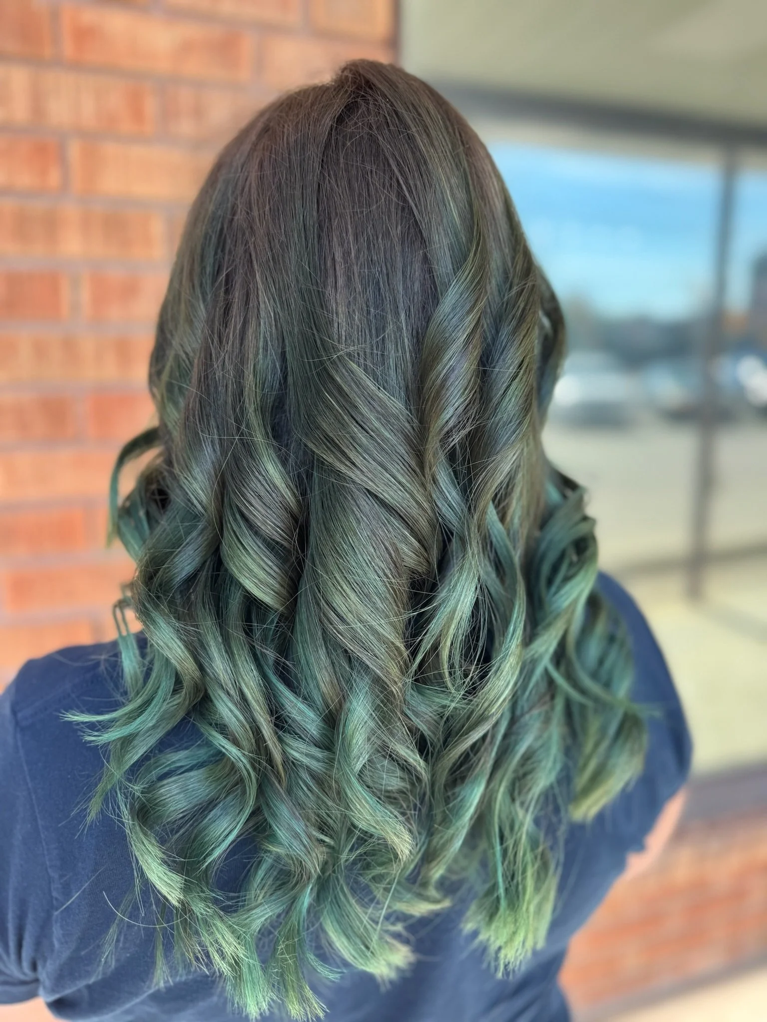 Back view of a person with long, wavy hair that has been colored with a greenish hue.