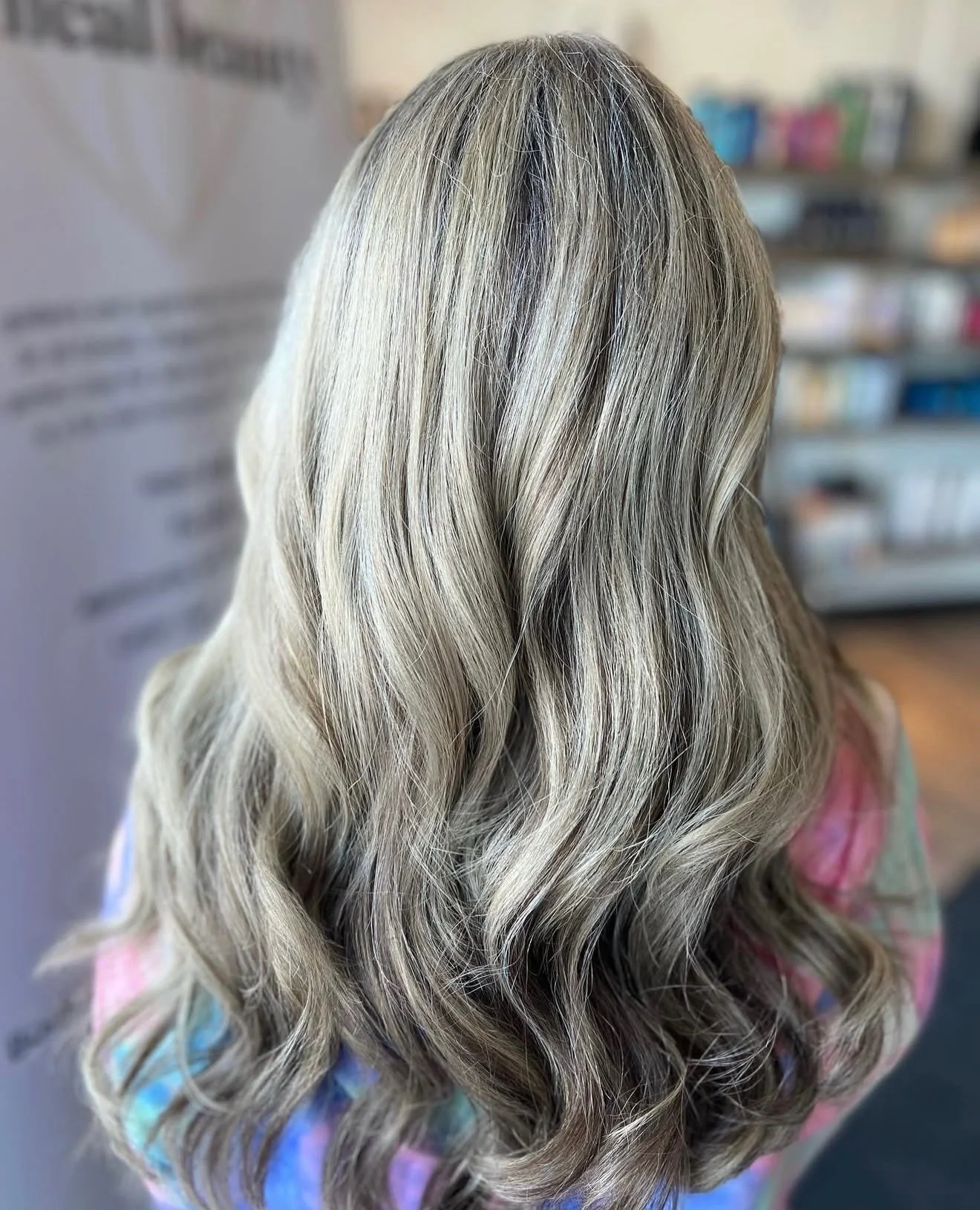 Back view of a woman with long, wavy, blonde hair in a salon or store setting.