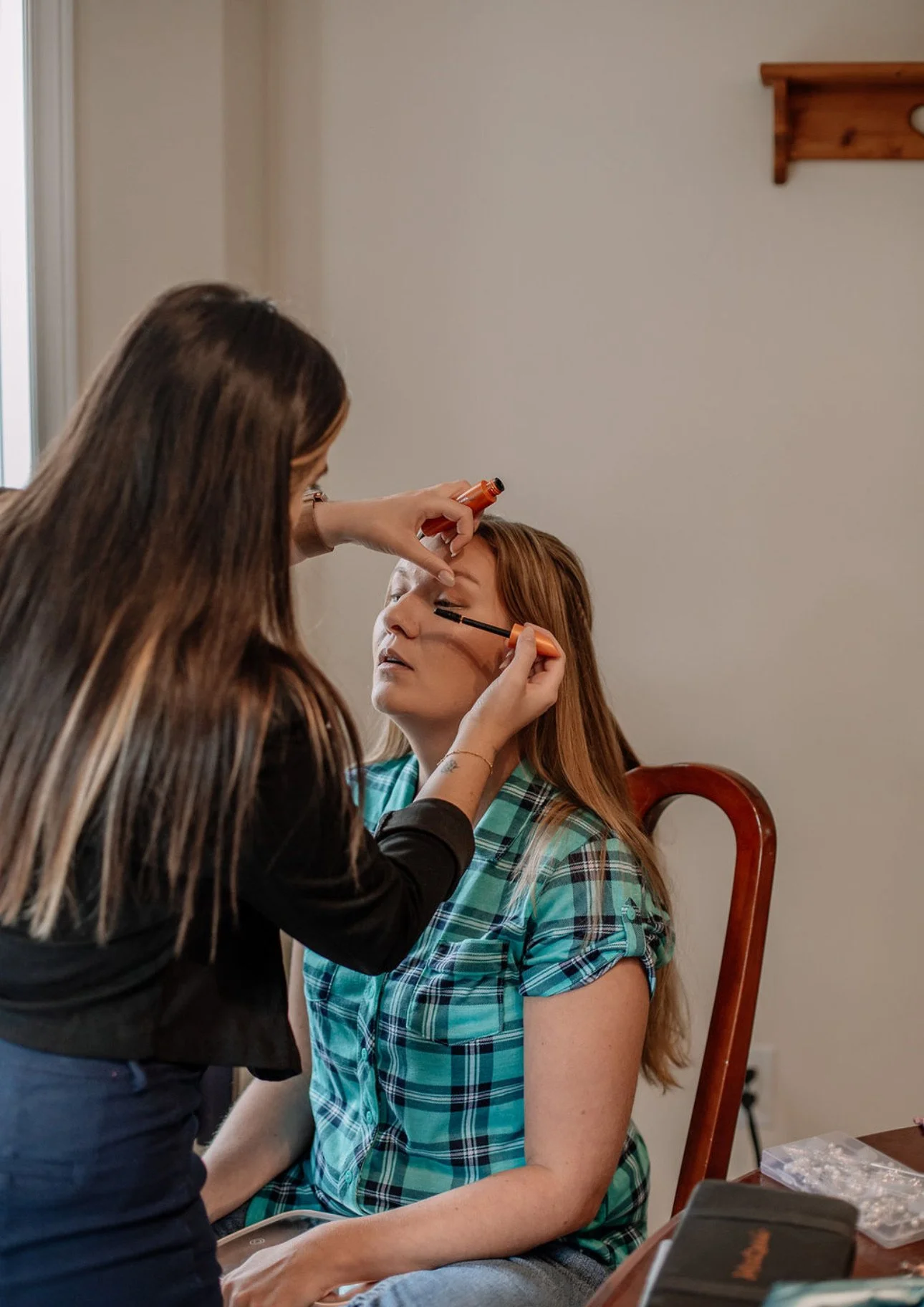 Woman sitting in a wooden chair having her makeup done by another woman